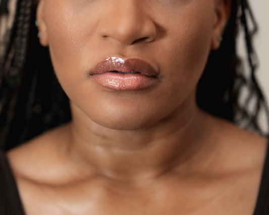 Close-up of a person's face with a focus on the lips wearing a glossy Luvelie lip product.